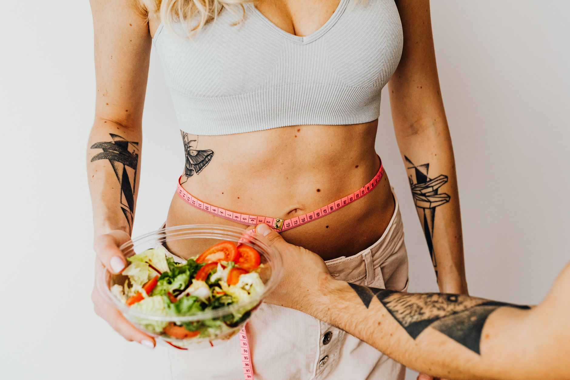 Fit woman measuring waist while holding a healthy salad bowl (Photo by www.kaboompics.com on Pexels)